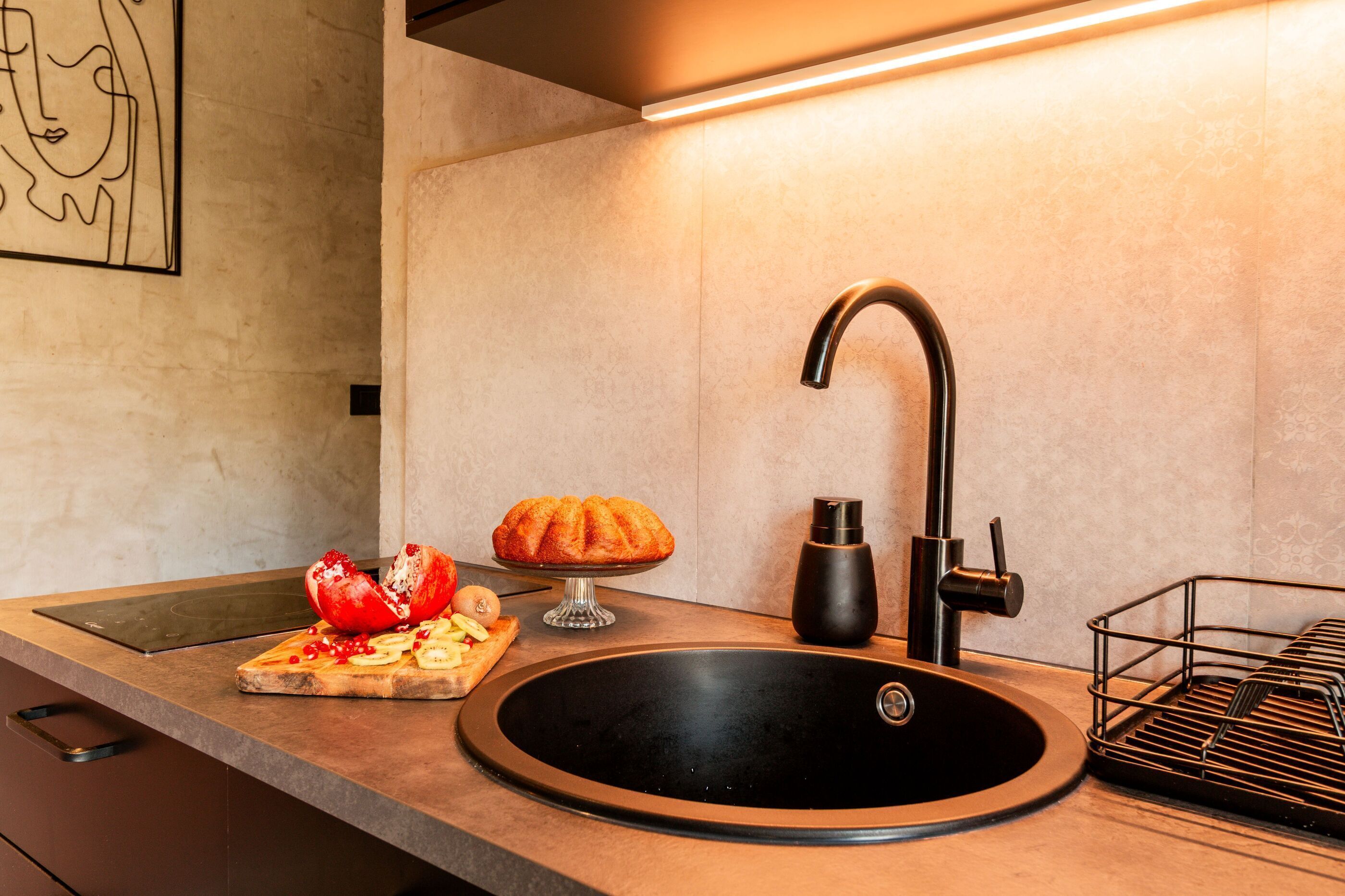 Une cuisine moderne avec un évier noir, un robinet en acier inoxydable et un plan de travail sur lequel on trouve une miche de pain, une tomate coupée et une planche à découper.
