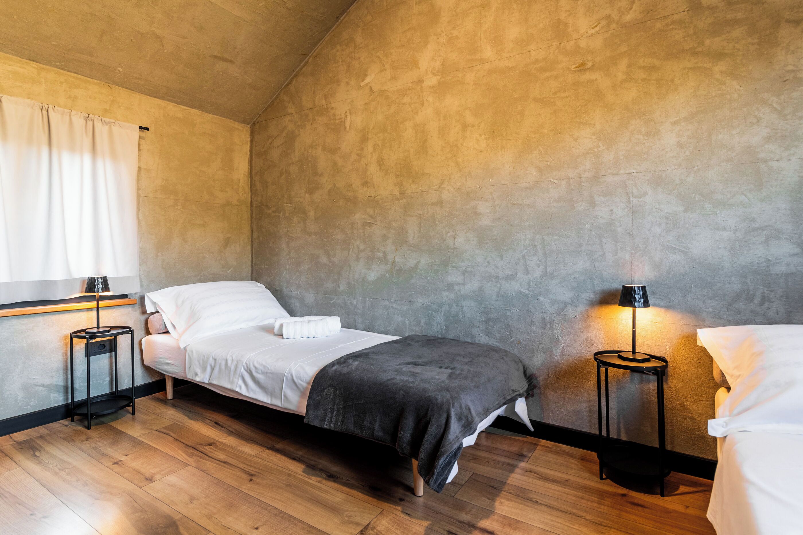 A bedroom with a single bed, a bedside table, a lamp, and a window with curtains.