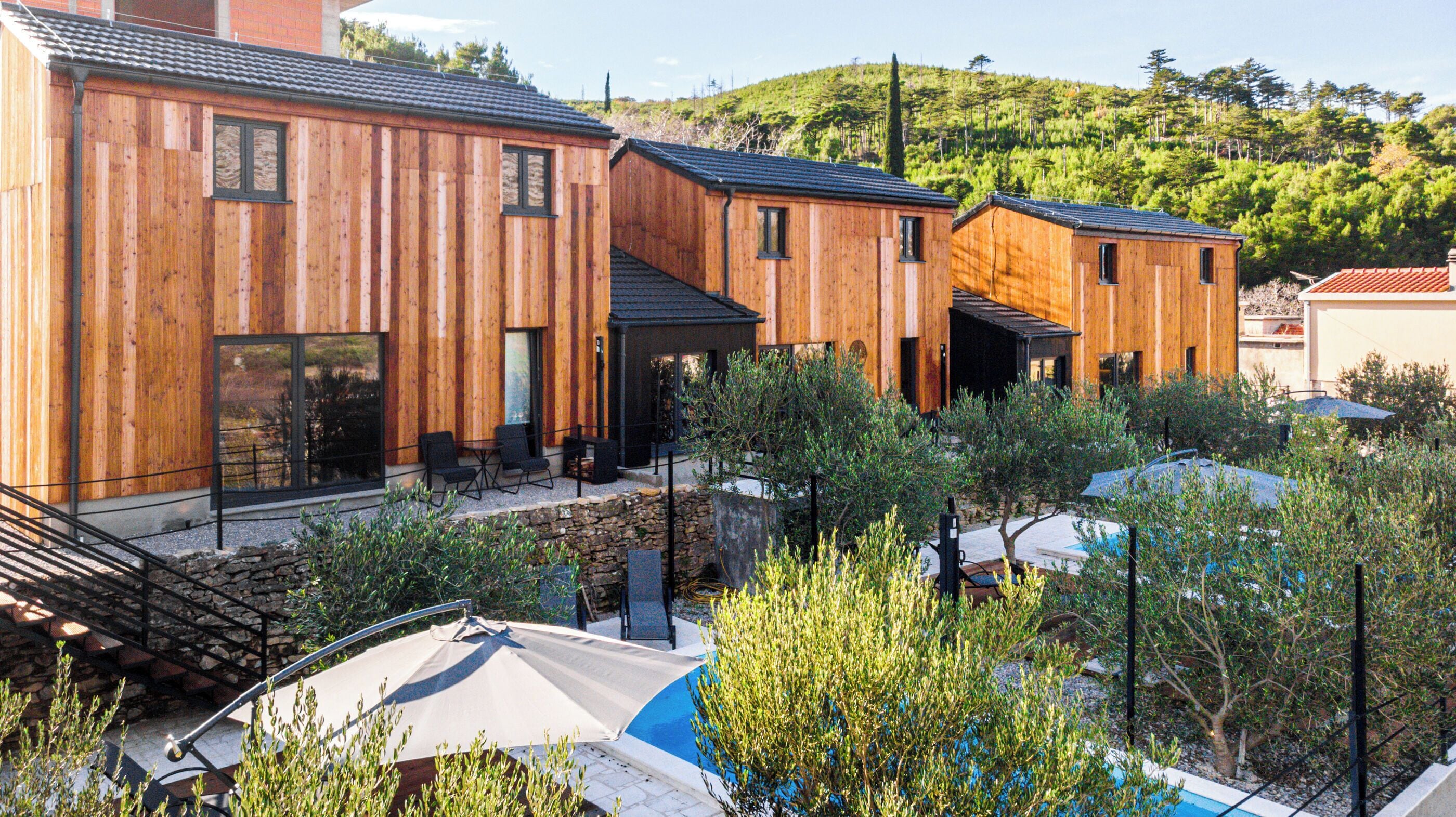 Un edificio moderno de madera con varias habitaciones, mobiliario exterior y una zona de piscina.