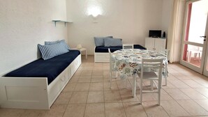 A compact room with a bed, a small table, a ceiling fan, and a TV. - Family Oasis: Pool and Garden - Baja Sardinia (Arzachena)