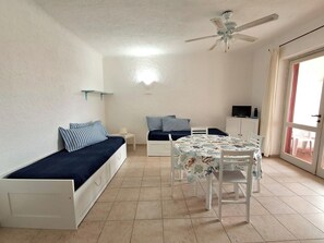 Ein gemütlicher Raum mit Bett, kleinem Tisch, Deckenventilator und Fernseher.
