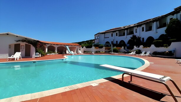 A pool with lounge chairs, a slide, and a building with arches. - Family Oasis: Pool and Garden - Baja Sardinia (Arzachena)