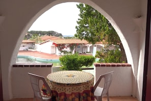 Ein Balkon mit Tisch und Stühlen, Blick auf einen Swimmingpool und ein Gebäude mit roten Ziegeldächern.