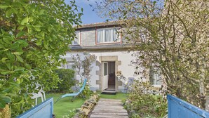 A pathway leading to a house with a stone facade, a wooden deck, and a garden with various plants. - House for 4 adults 2 kids, walk everywhere (Ile Tudy)