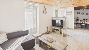 A living room with a sofa, coffee table, TV, and a dining area with chairs and a table. - House for 4 adults 2 kids, walk everywhere (Ile Tudy)