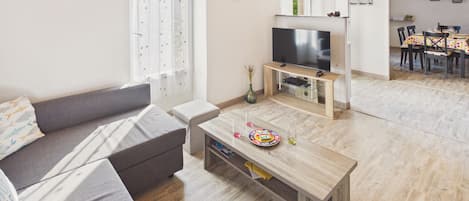 Un salon comprenant un canapé, une table basse, un téléviseur et un coin repas avec des chaises et une table.