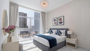 Un dormitorio moderno con una cama grande, una mesita de noche, un florero con flores y vistas a la ciudad a través de un ventanal amplio.