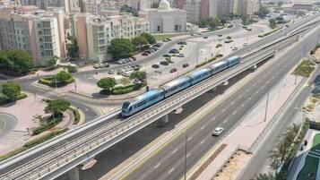 Un tren en una vía elevada, una carretera con varios carriles y edificios circundantes.