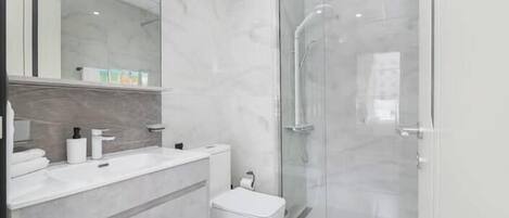 A modern bathroom with a glass shower enclosure, a white sink, and a toilet.