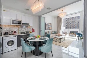 A modern kitchen with a microwave, washing machine, and dining area with chairs and a table. - Vogue | Pearlz by Danube near Ibn Battuta Mall (Dubai)