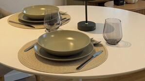 Una mesa de comedor con platos, cubiertos y una lámpara, frente a una pared con un espejo que refleja una cama y una ventana.