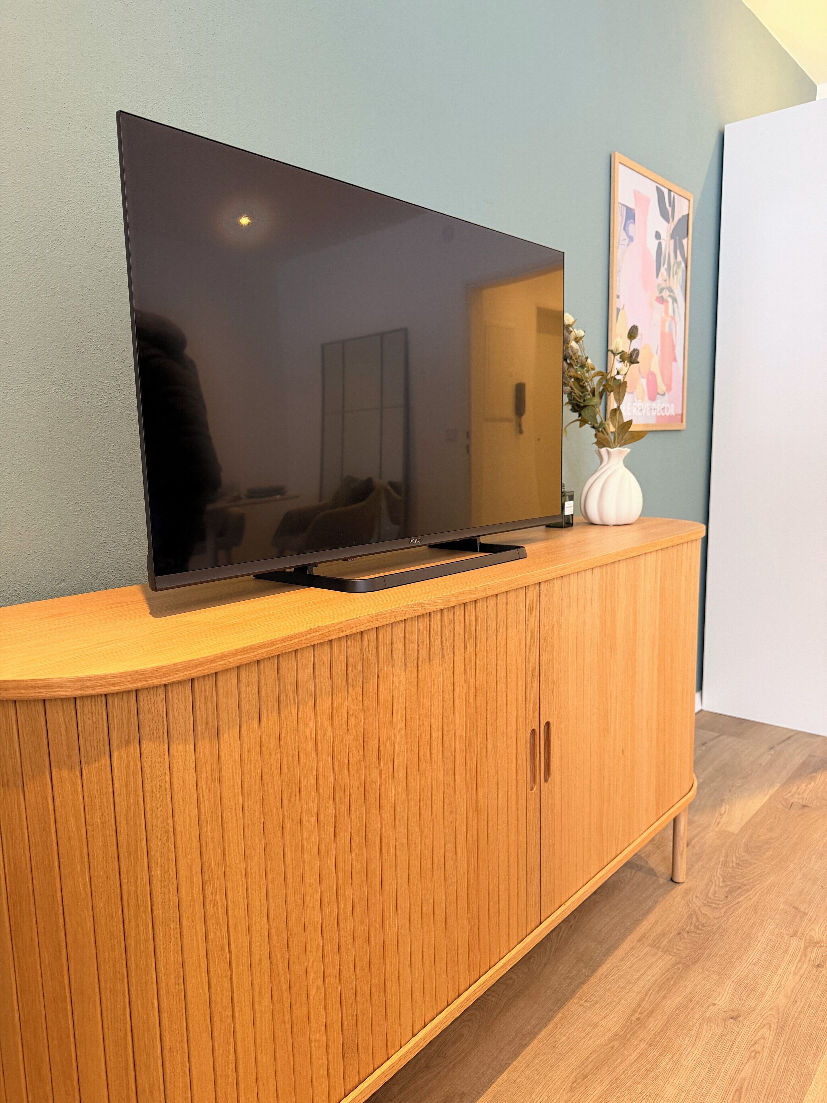 A flat-screen TV mounted on a wooden cabinet with a vase of flowers on top.