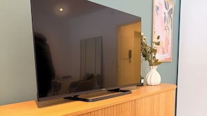 Un televisor de pantalla plana montado en un mueble de madera con un florero encima.