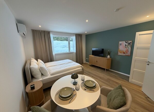 A compact room with a bed, a dining table with plates, a TV, and a cabinet.