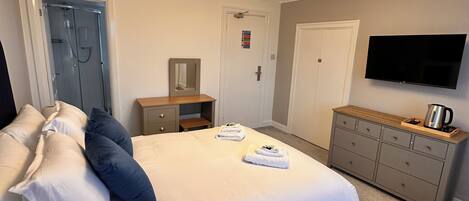 A hotel room with a large bed, a dresser, a television, and a shower.