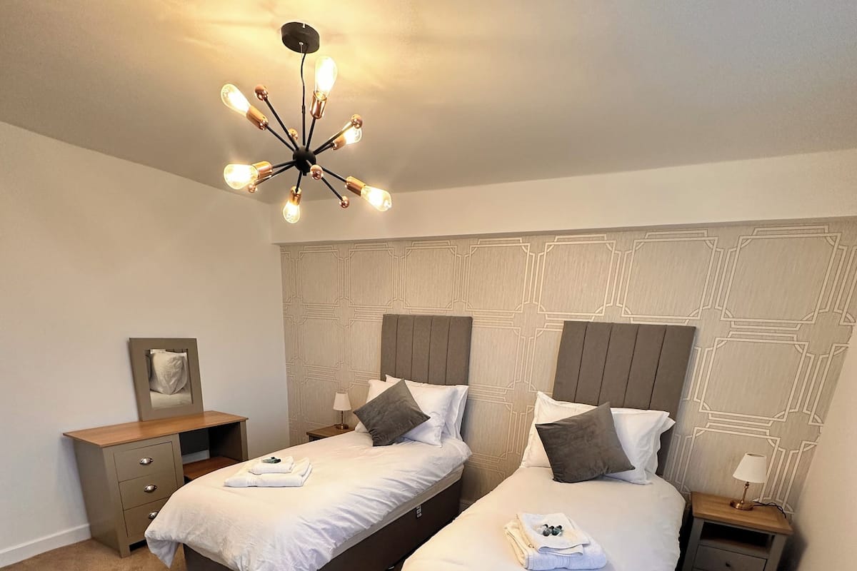 Une chambre d’hôtel avec deux lits, un miroir, des tables de chevet et un lustre moderne.