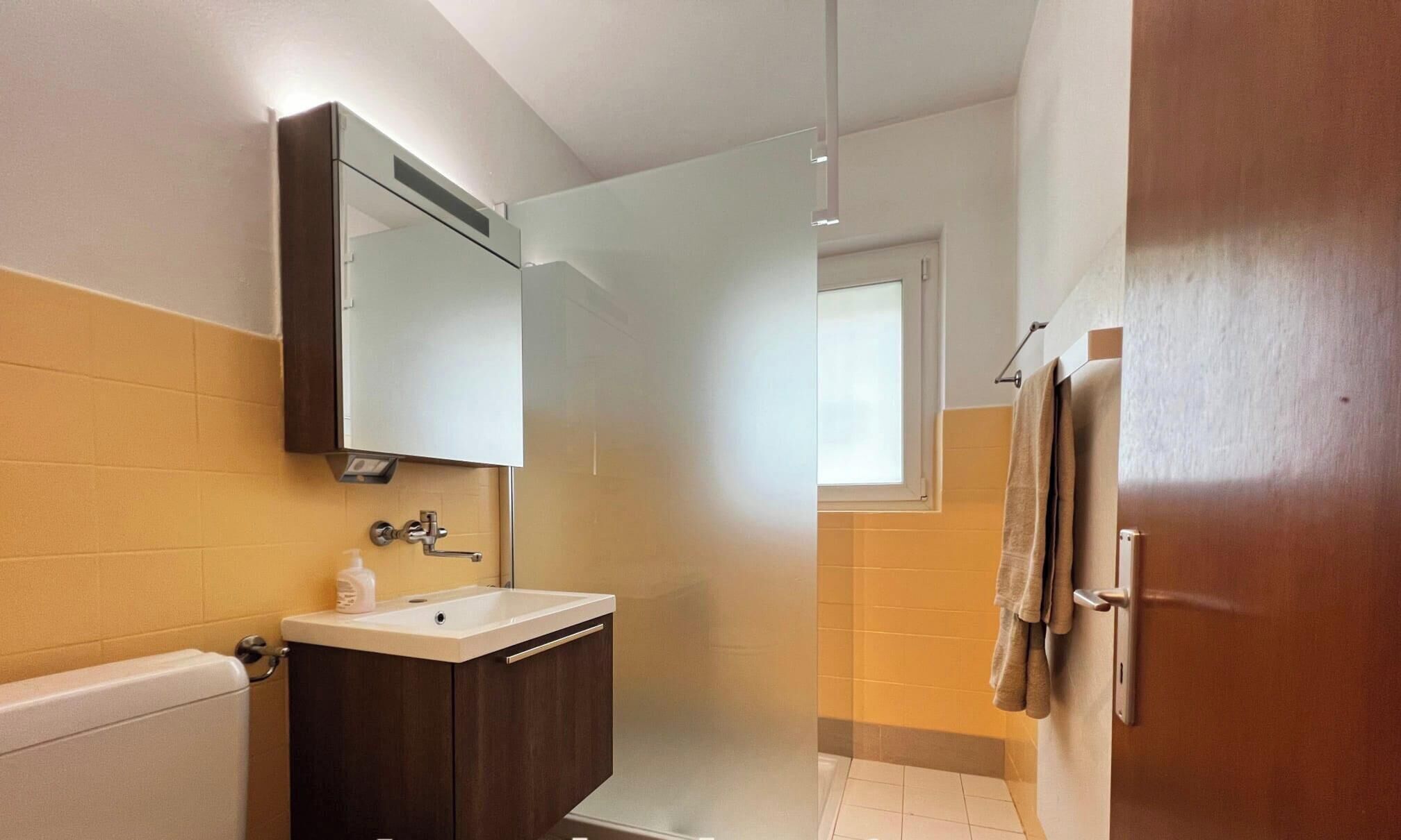A bathroom with a sink, mirror, towel rack, and a door leading to another room.