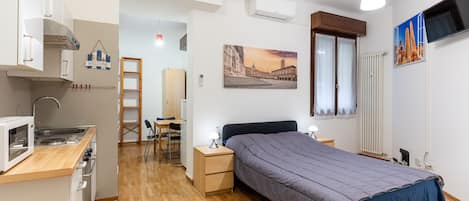 Ein kompakter Raum mit Bett, Schreibtisch, Stuhl, einer Mikrowelle und einer kleinen Küchenzeile.