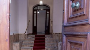 Un escalier recouvert d’une moquette rouge menant à une porte ornée de panneaux en bois.