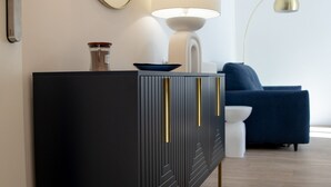 Un salon moderne avec une console noire, un miroir rond, une lampe et un canapé bleu.