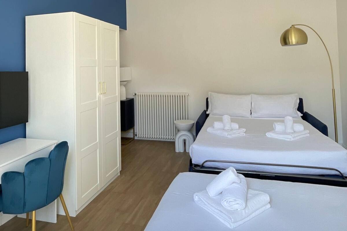 Ein Hotelzimmer mit Bett, Schreibtisch, Kleiderschrank, Heizkörper und einer Deckenleuchte.