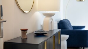 Une pièce moderne avec une console noire, un vase en verre, une lampe blanche, une chaise bleue et un miroir avec un cadre doré.