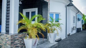 A house with a porch, potted plants, and a brick base. - Livin Lagos Shortstays (Lekki)