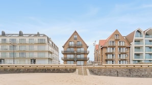 Ein Hotel direkt am Strand mit mehreren Etagen, Balkonen und einer Treppe, die zum Strand führt.