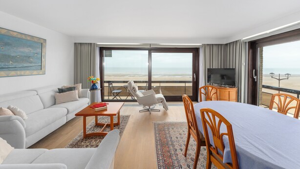 Ein Hotelzimmer mit Balkon, einer Couch, einem Esstisch, einem Fernseher und Blick auf den Strand.