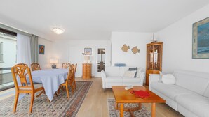 Ein Wohnzimmer mit Essbereich, weißen Möbeln, einer Chandelier und Blick durch ein Fenster.