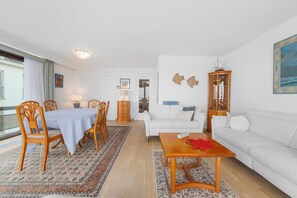 Ein Wohnzimmer mit Essbereich, weißen Möbeln, einer Chandelier und Blick durch ein Fenster.