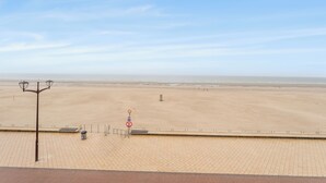 Blick auf einen Strand mit gepflastertem Weg, einer Straßenlaterne und einem Schild, das das Schwimmen verbietet.