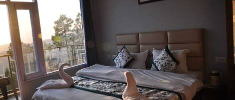 A bedroom with a large bed, two swan-shaped pillows, a headboard, a window with a view, and a framed picture on the wall.