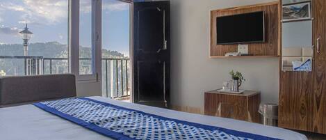 A bedroom with a large bed, a TV mounted on the wall, and a view of a tower through a window.