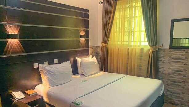 A hotel room with a bed, bedside lamps, a telephone, and a window with curtains. - Green House Hotel And Suites (Lagos)
