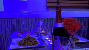 A table set with a bottle of champagne, rose petals, and two dishes of food. - Green House Hotel And Suites (Lagos)