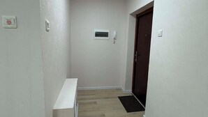 A hallway with a light fixture, a bench, a door, and a thermostat on the wall. - 44 Prime Location 1BR | New Furniture (Ulaanbaatar)