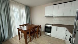 A compact kitchen with a dining table, white cabinets, a stove, and a refrigerator. - 44 Prime Location 1BR | New Furniture (Ulaanbaatar)
