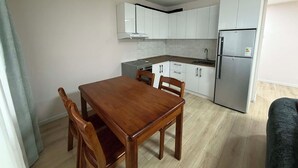 A compact kitchen with white cabinets, a dining table, and a refrigerator. - 44 Prime Location 1BR | New Furniture (Ulaanbaatar)