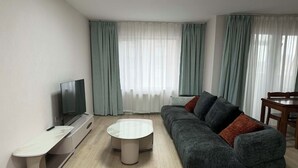 A modern living room with a sofa, a coffee table, a TV, and a dining table. - 44 Prime Location 1BR | New Furniture (Ulaanbaatar)