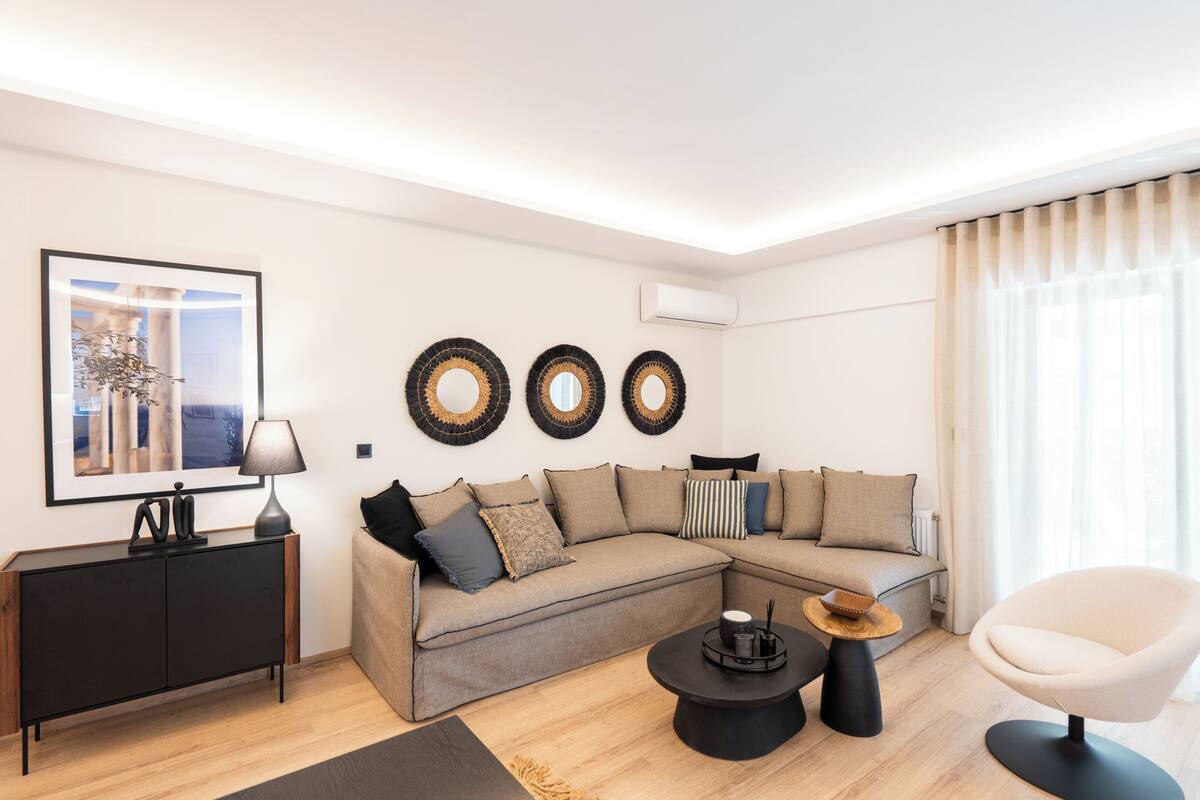 A modern living room with a sectional sofa, a round coffee table, a side table, and a chair. There is a framed picture on the wall, a lamp, and three wall-mounted decorative items.