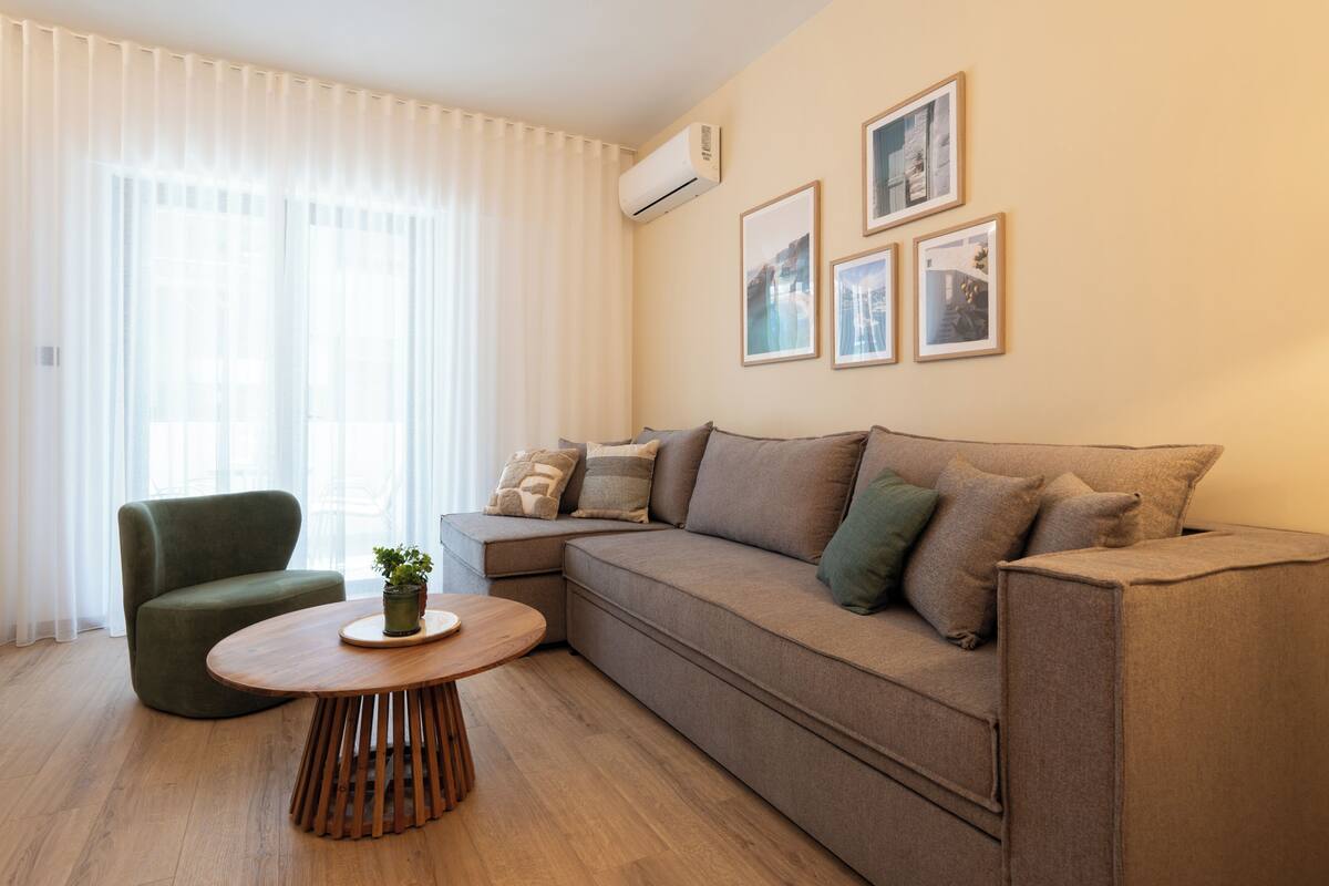 A living room with a sofa, a round wooden table, a chair, and a potted plant.