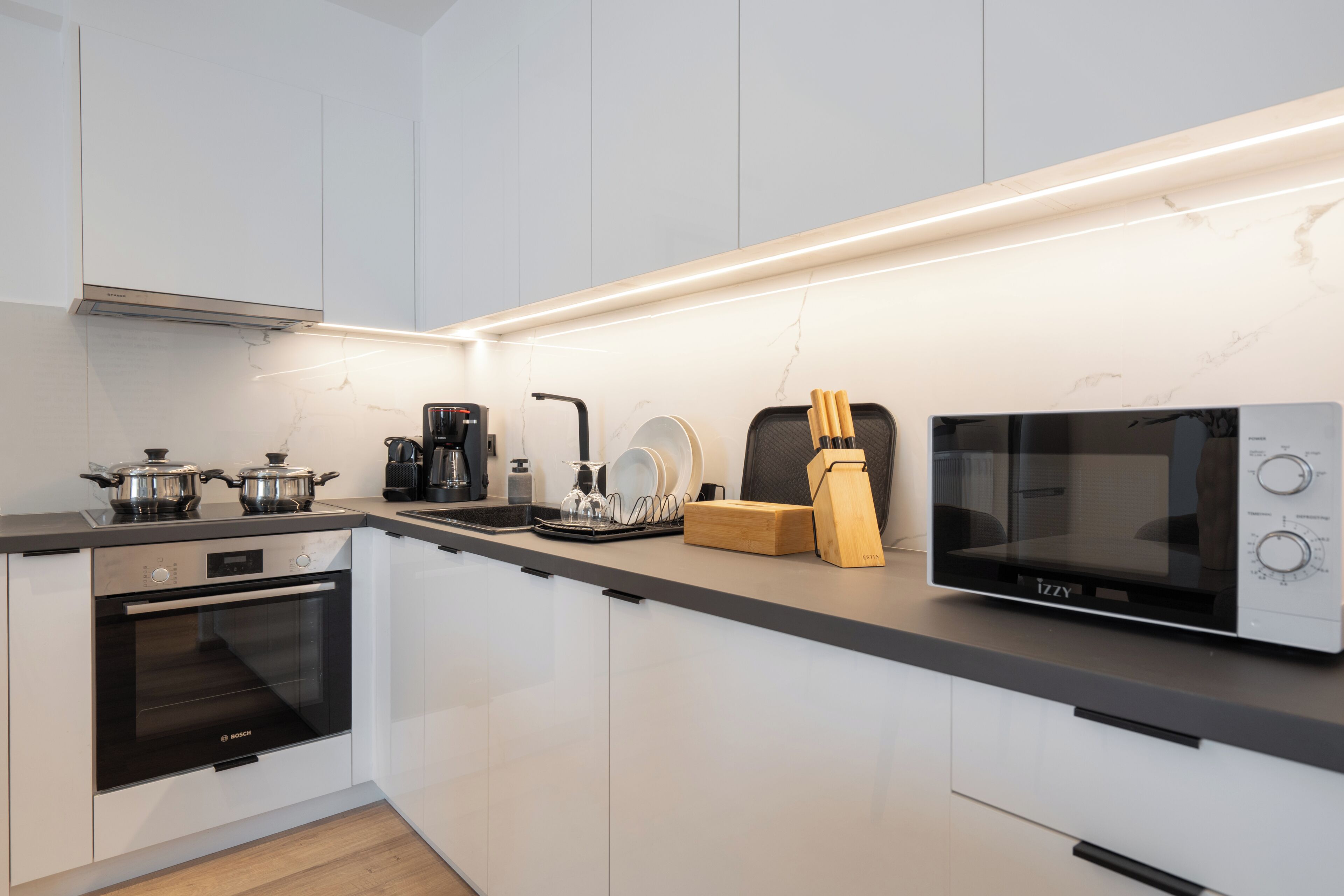 Een moderne keuken met een Bosch oven, een Izzy magnetron, een koffiezetapparaat en een messenblok.