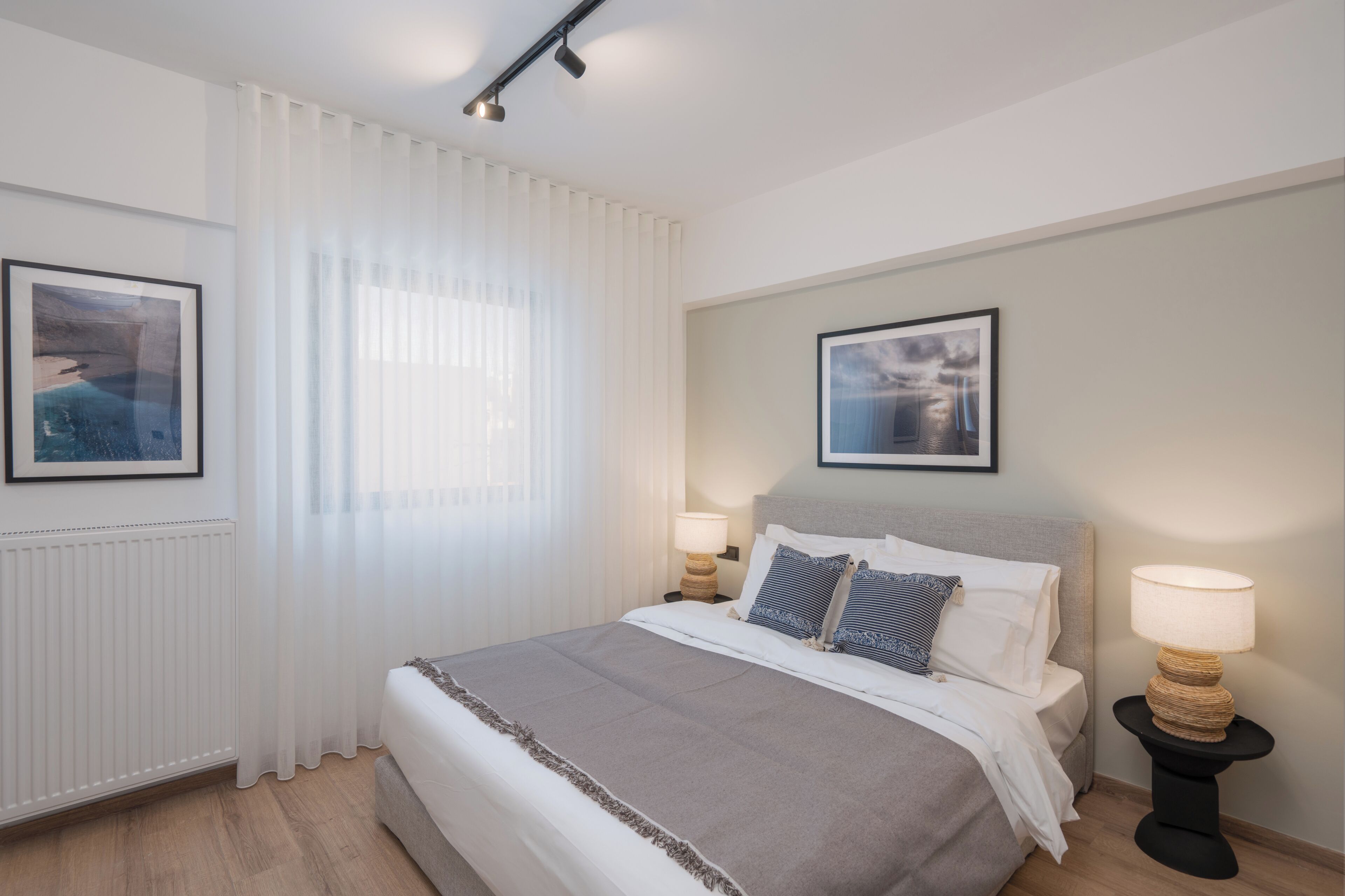 A neatly arranged bedroom with a bed, two bedside tables, a window with curtains, and two framed pictures on the walls.