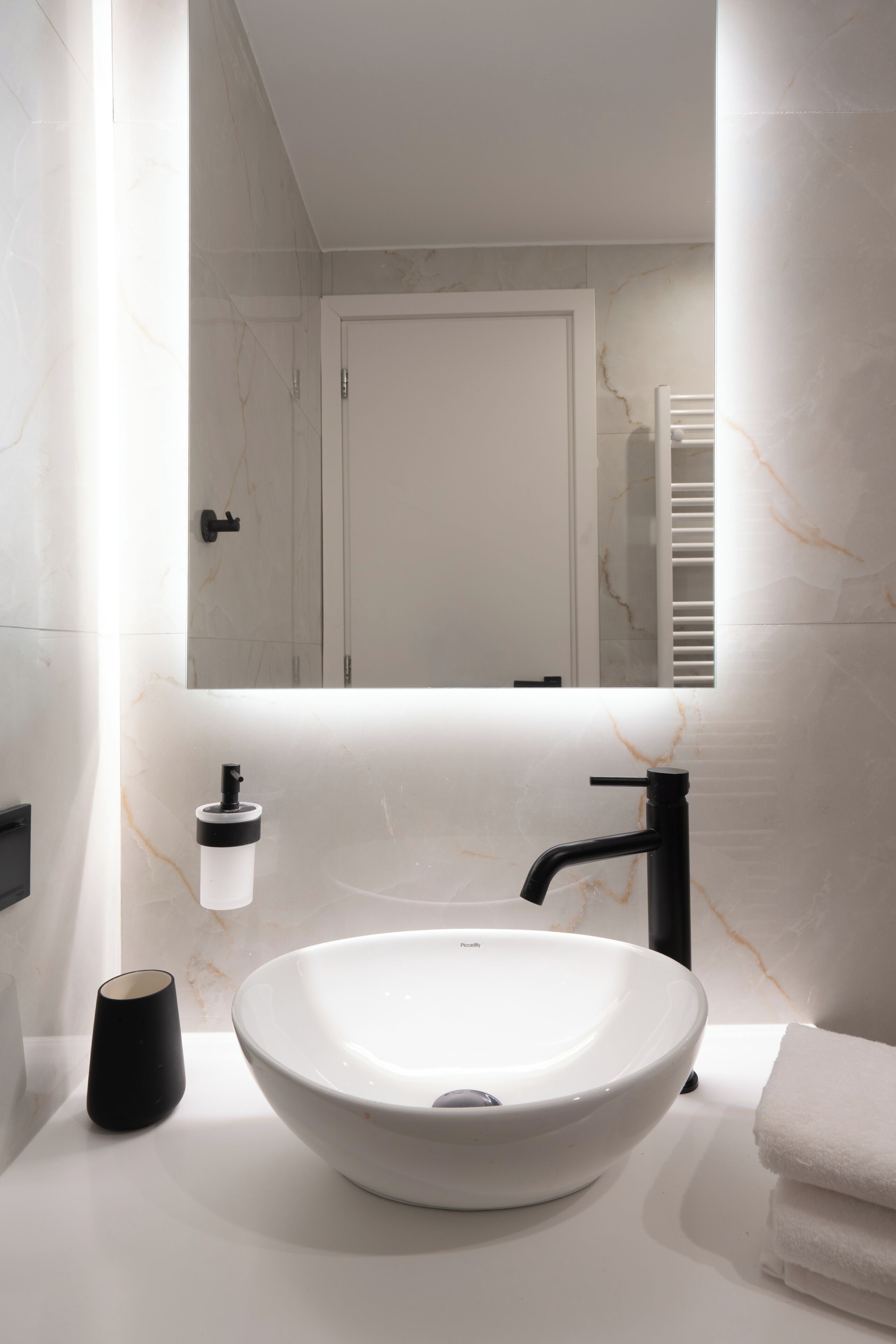 A modern bathroom with a large white basin, a black faucet, a towel rack, and a small black container.