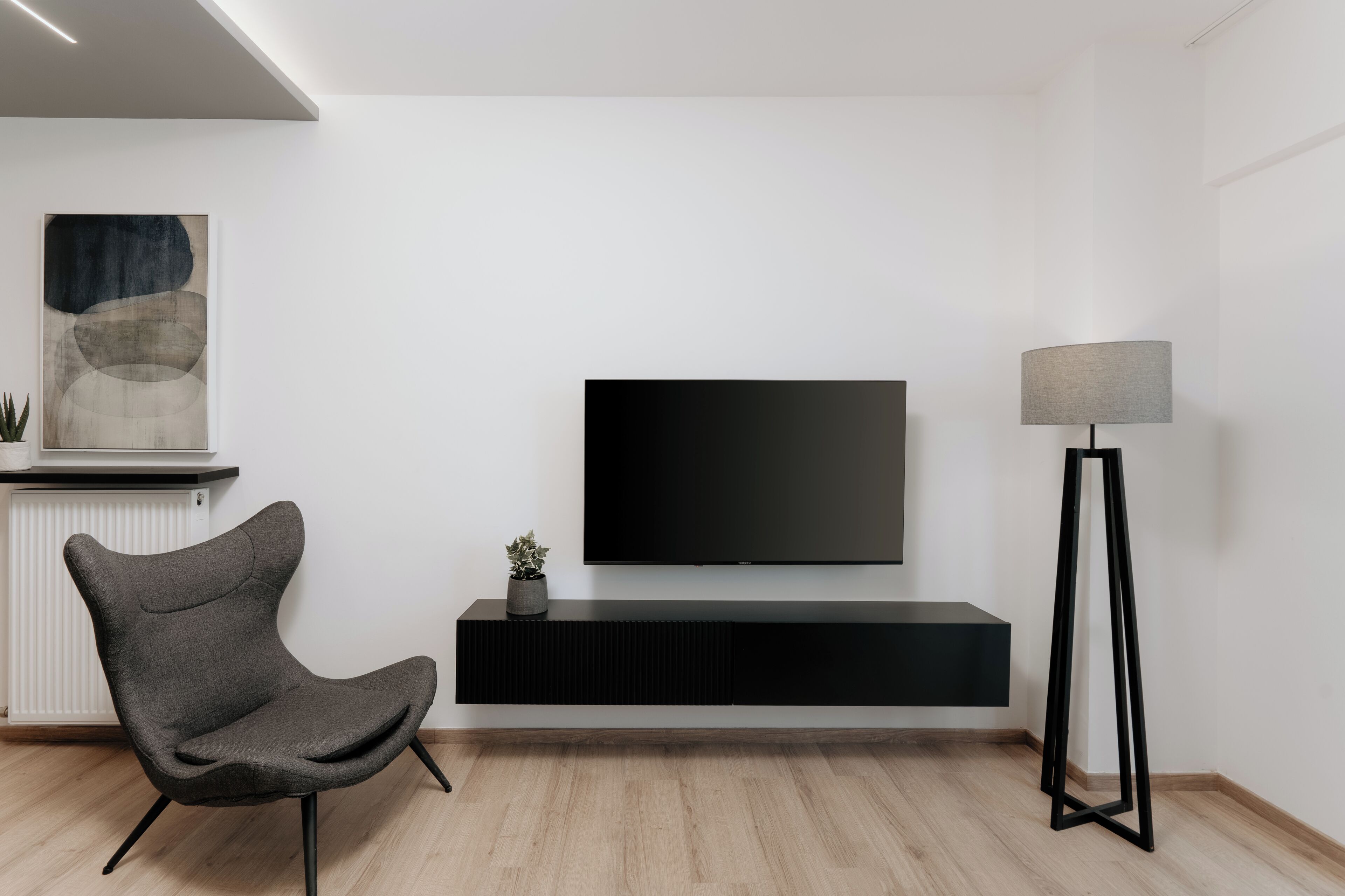 A modern living room with a flat-screen TV, a dark grey chair, a floor lamp, and a minimalist design.