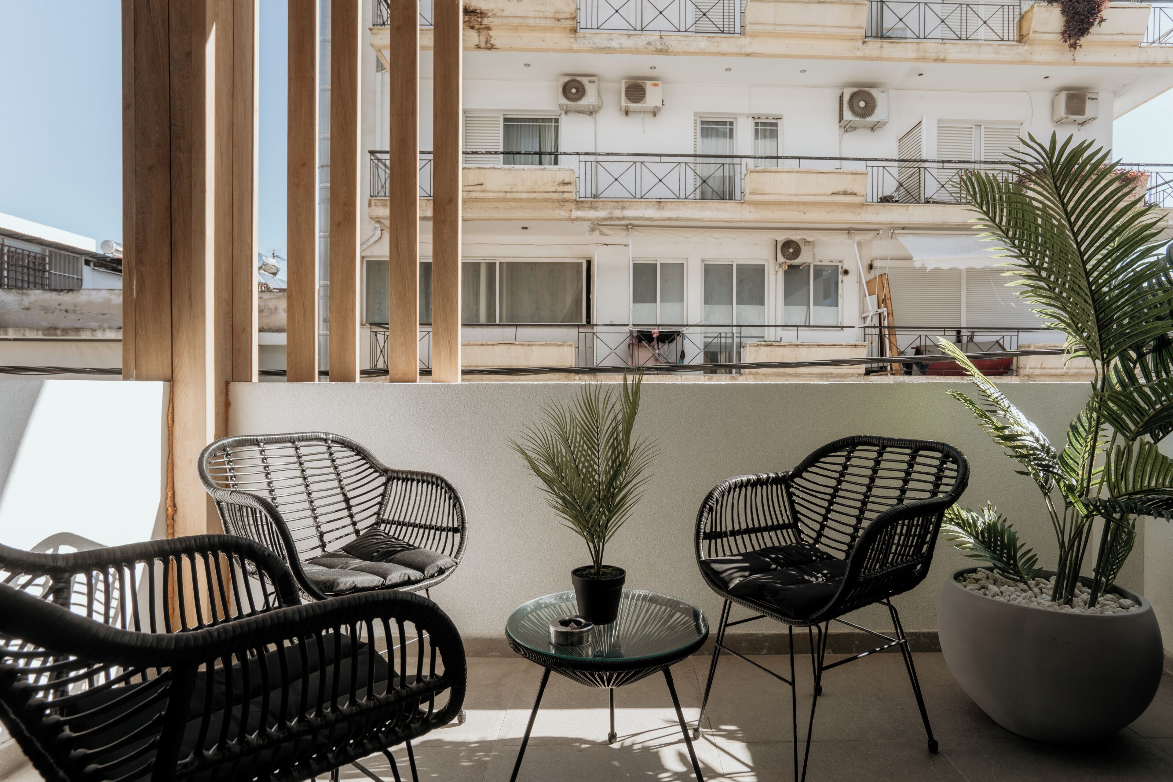 Un balcon avec deux fauteuils en osier noir, une petite table en verre et un pot de fleurs.