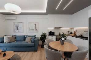 A modern living room with a sofa, a dining table with chairs, and a kitchen area with cabinets and appliances. - The Edge Piraeus Luxury Residences (Piraeus)