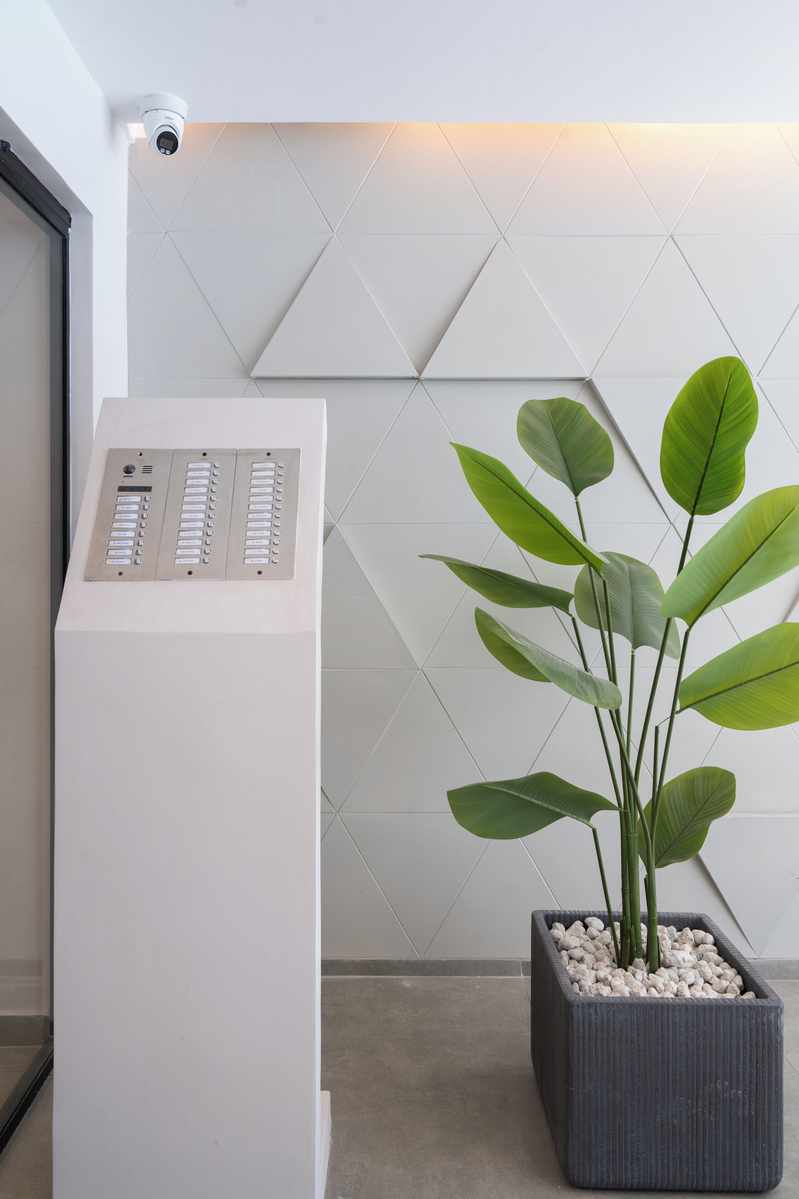 A reception desk with a security camera, a potted plant, and a geometric wall design.