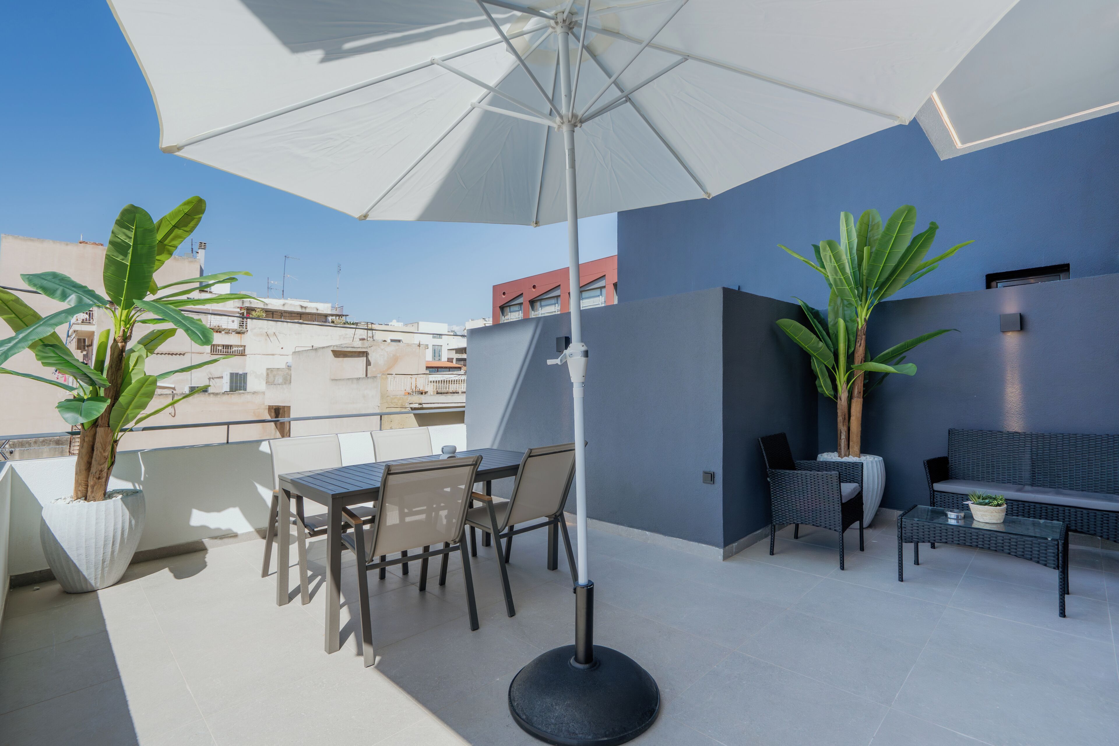 Une terrasse sur le toit, avec une table et des chaises, un grand parasol et des plantes en pot.
